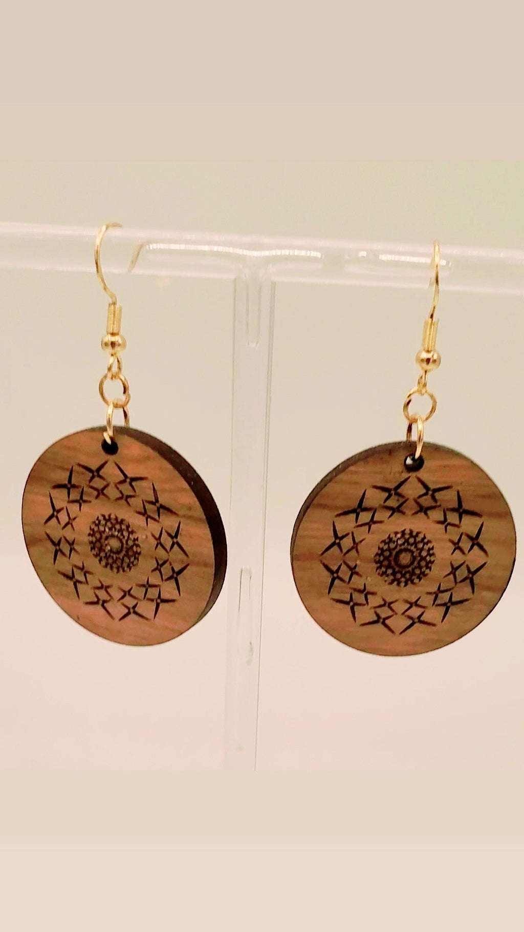 Wooden earrings with star patterns on a clear stand against a beige background